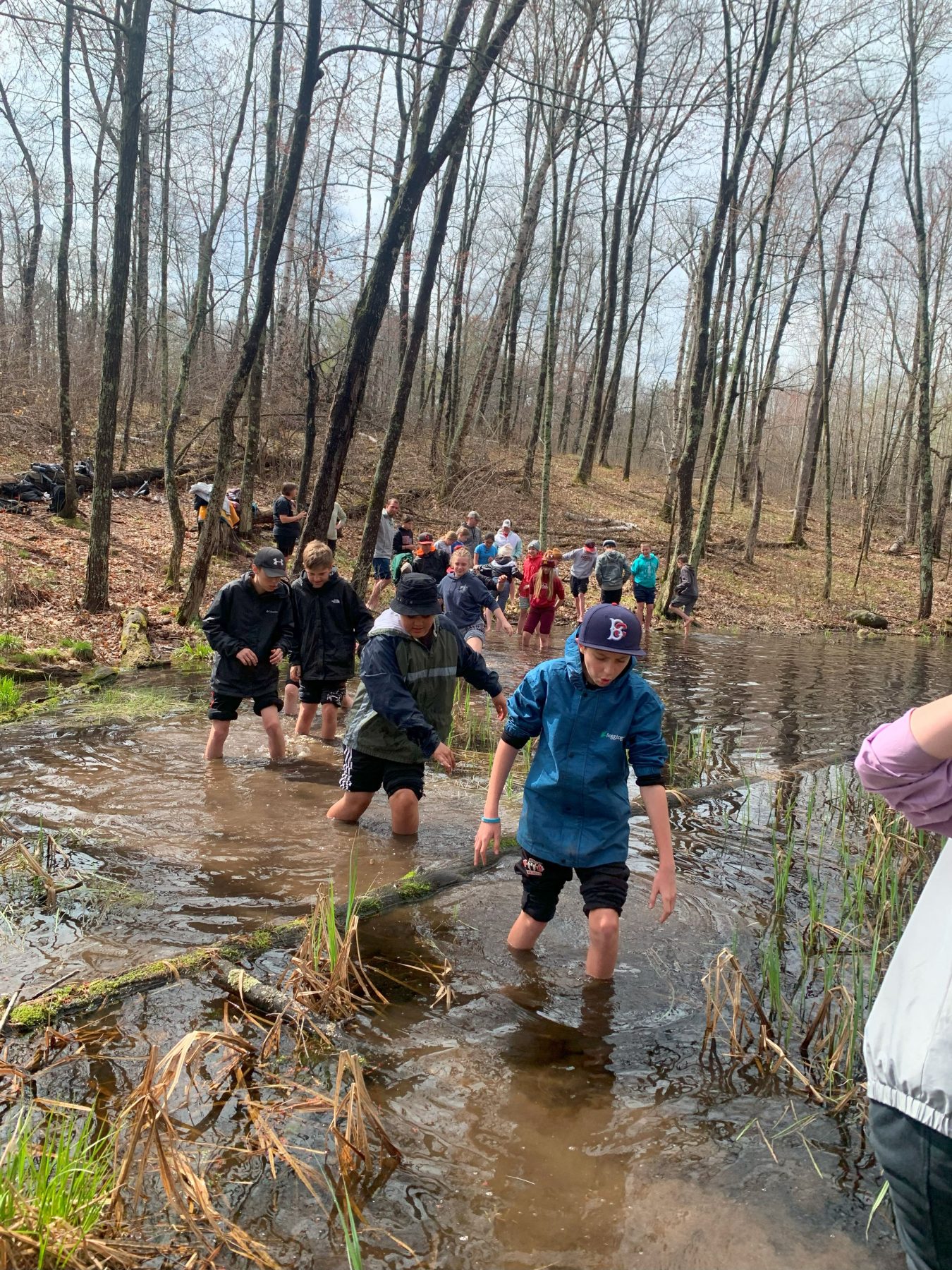 Campers walk through knee deep muddy water in a line in the woods of Camp Foley