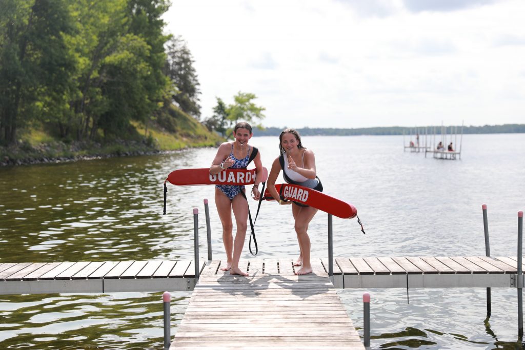 2 girls on the Camp Foley swim dock with life guard tubes and whistles in their mouth 