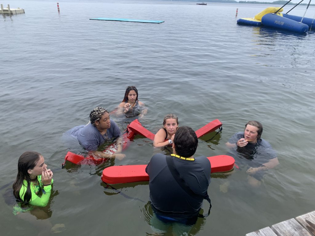 Campers in the water with life guard tubes receive instruction from a counselor 