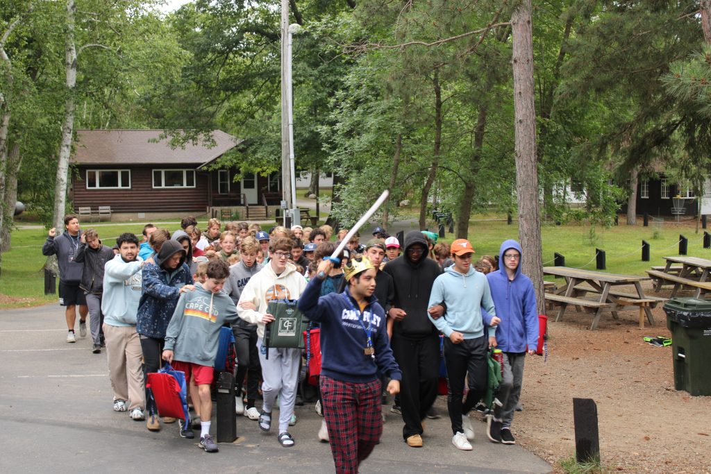 male counselor leading group of boys with foam sword held high 
