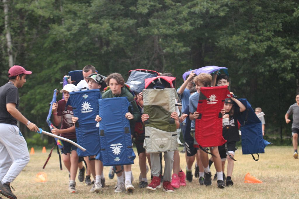 Campers holding chairs like shields and running forward 