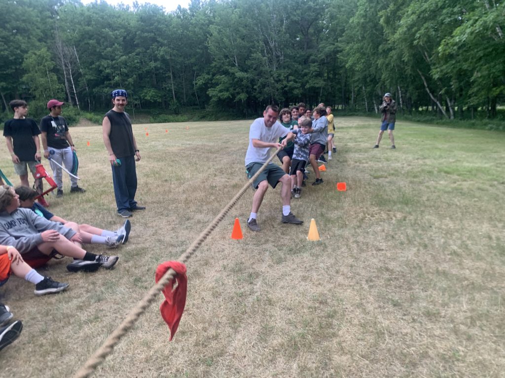 Campers playing tug of war while people watch 