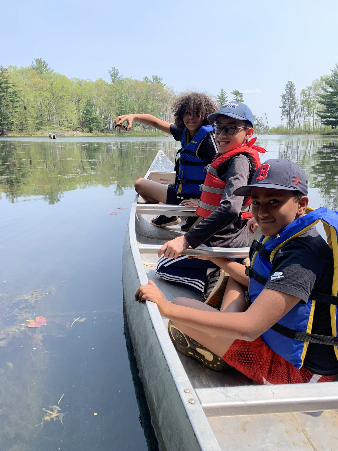 3 kids sitting in a canoe, one child is holding a turtle on Hidden Lake at Camp Foley 
