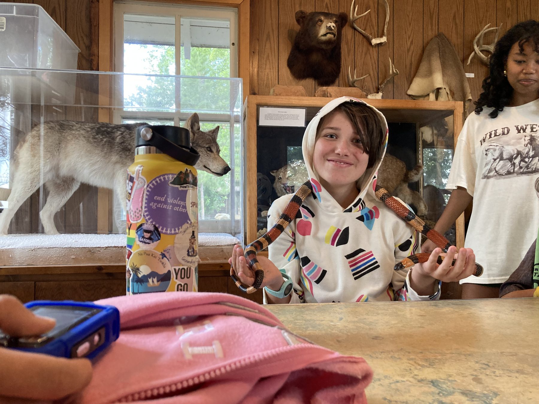 A camper holds a snake around their shoulders with a stuffed wolf in the background 
