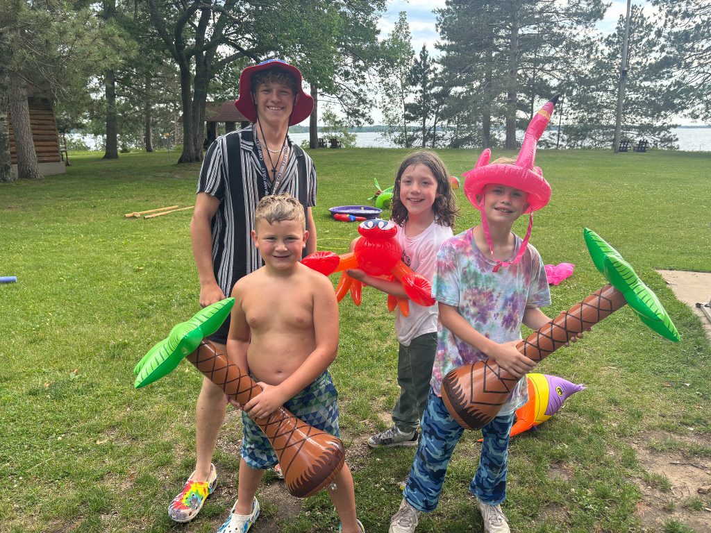 3 camp foley campers and a counselor smile and hold inflatable pool toys 