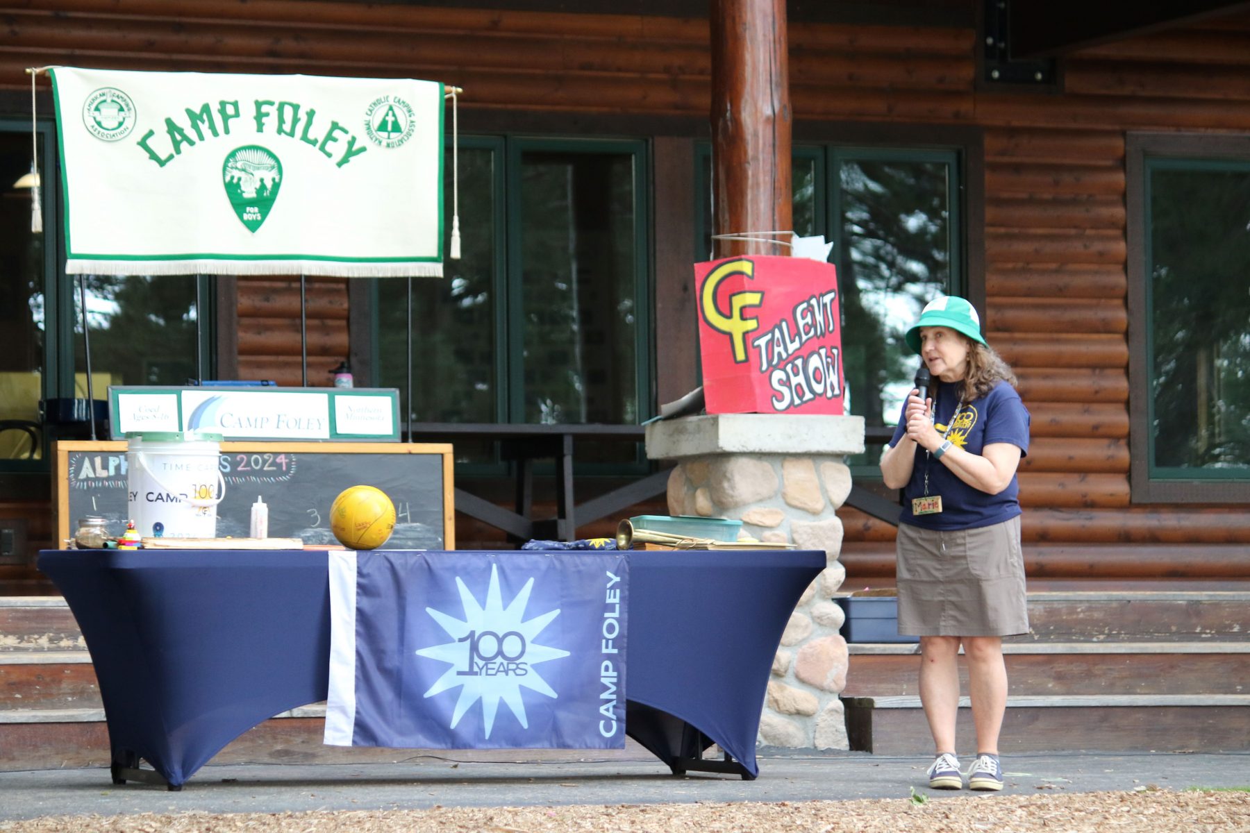 A woman stands in front of a display table with a flag that says Camp Foley 100 years 