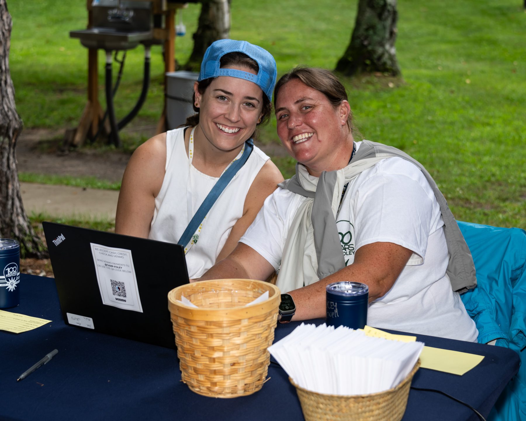 two women sit at a table in front of a laptop smiling at the camera