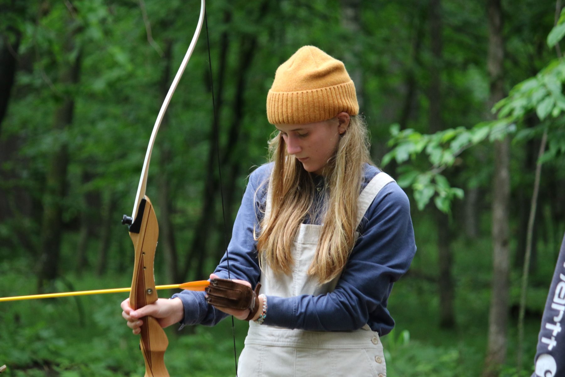 A girl holds a bow and loads an arrow into it on the Camp Foley archery field 