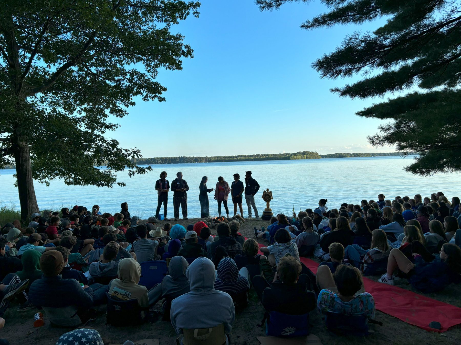 A group of camp counselors pose in front of a red carpet at a campfire performance 