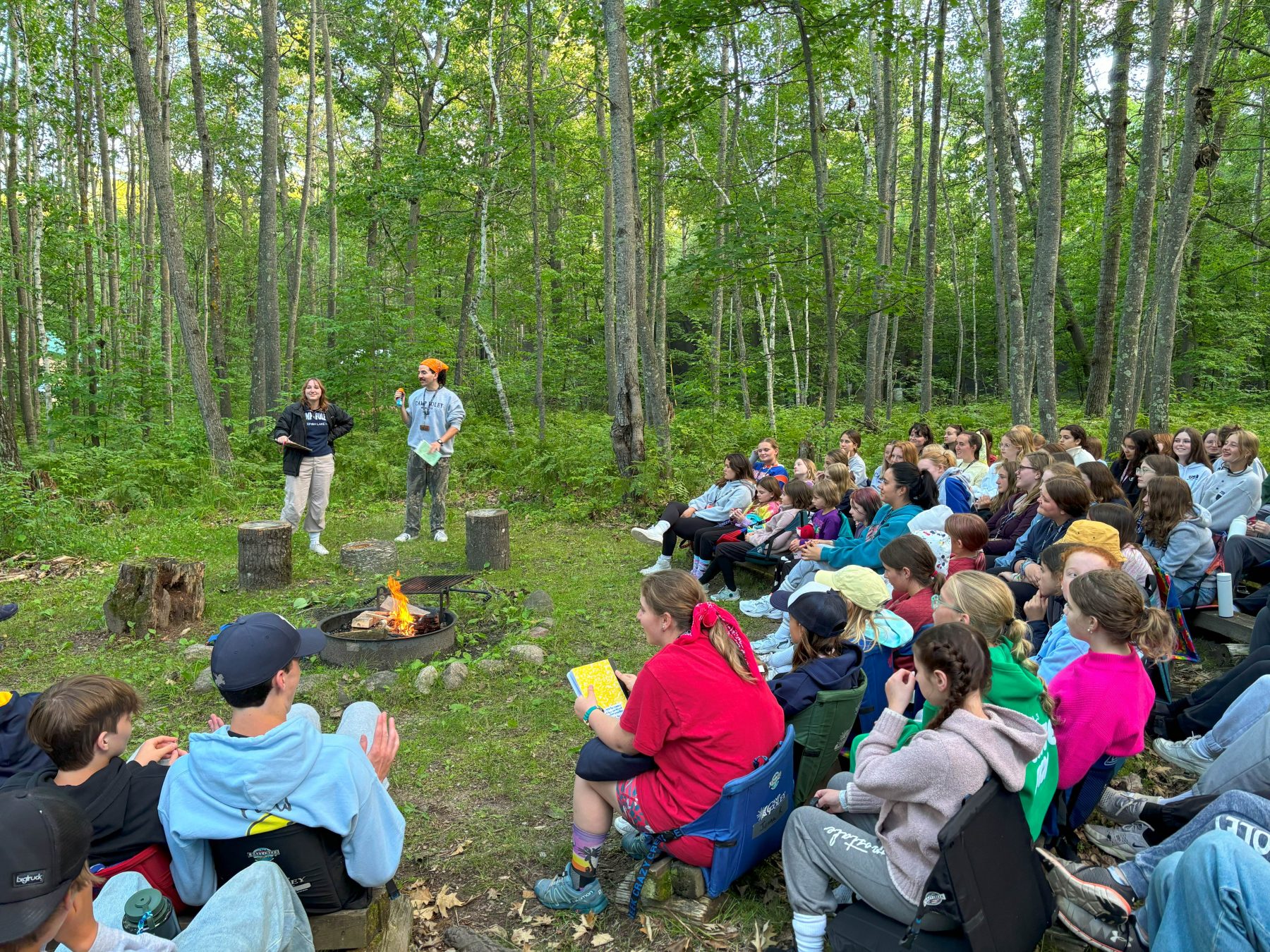 2 people stand in front of crowd leading a campfire at Camp Foley 