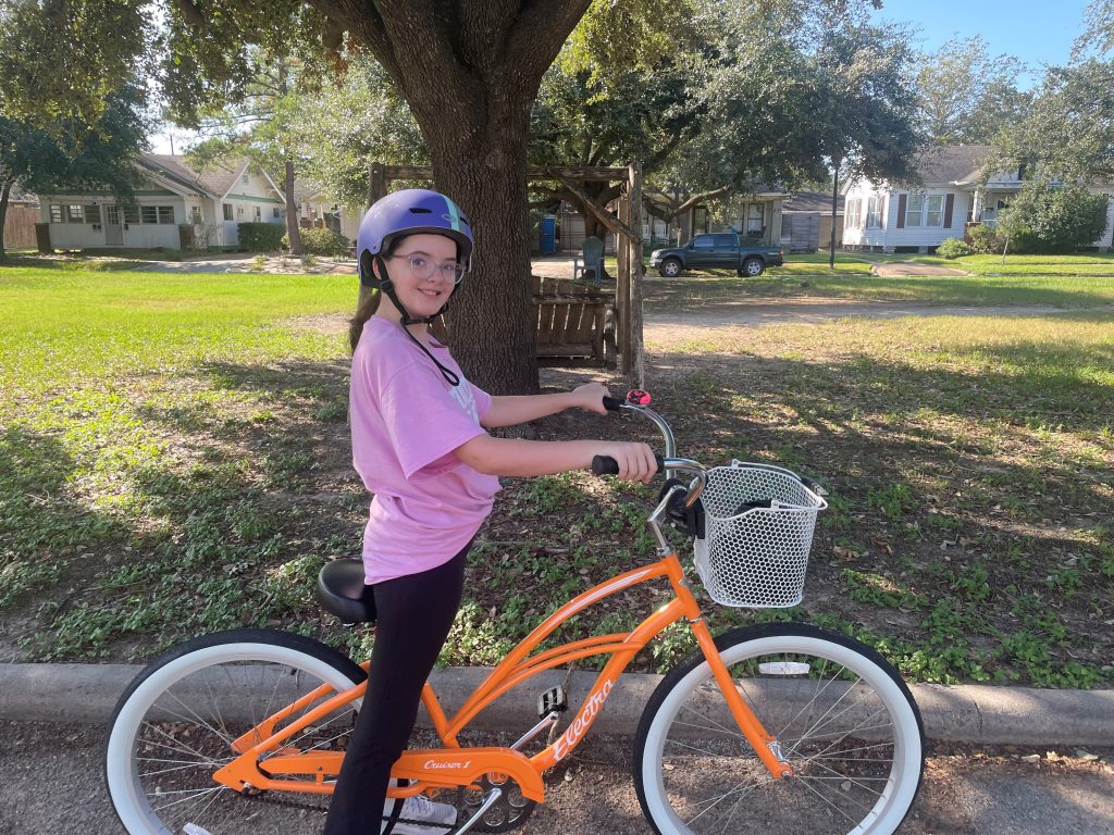 A girl poses with an orange bike 