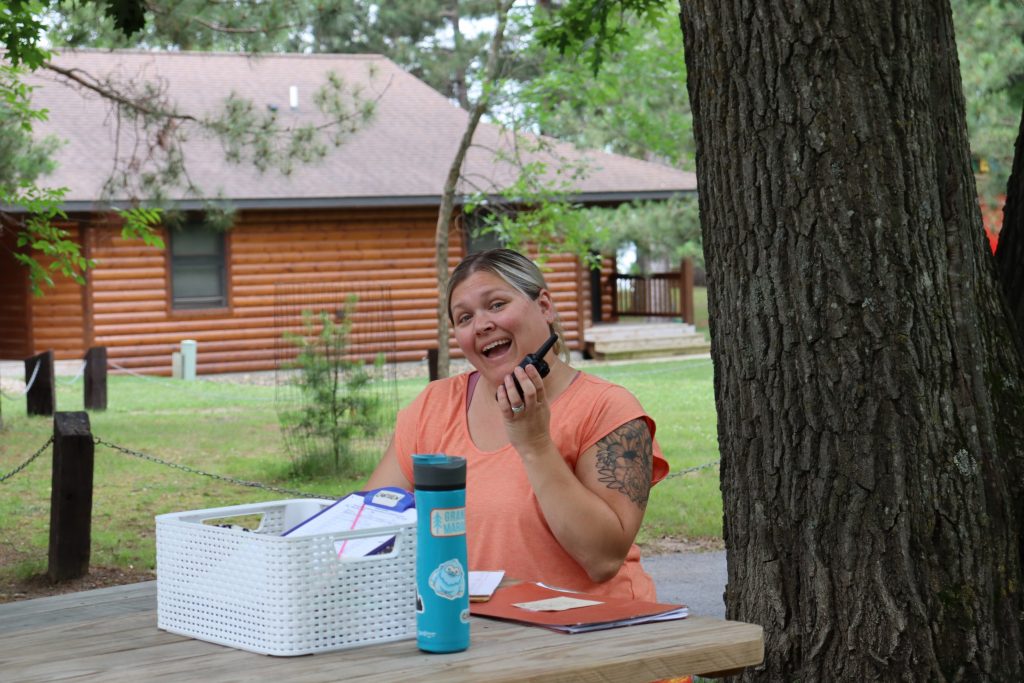 A camper coordinator sits at picnic table at Camp Foley talking into a walkie talkie 