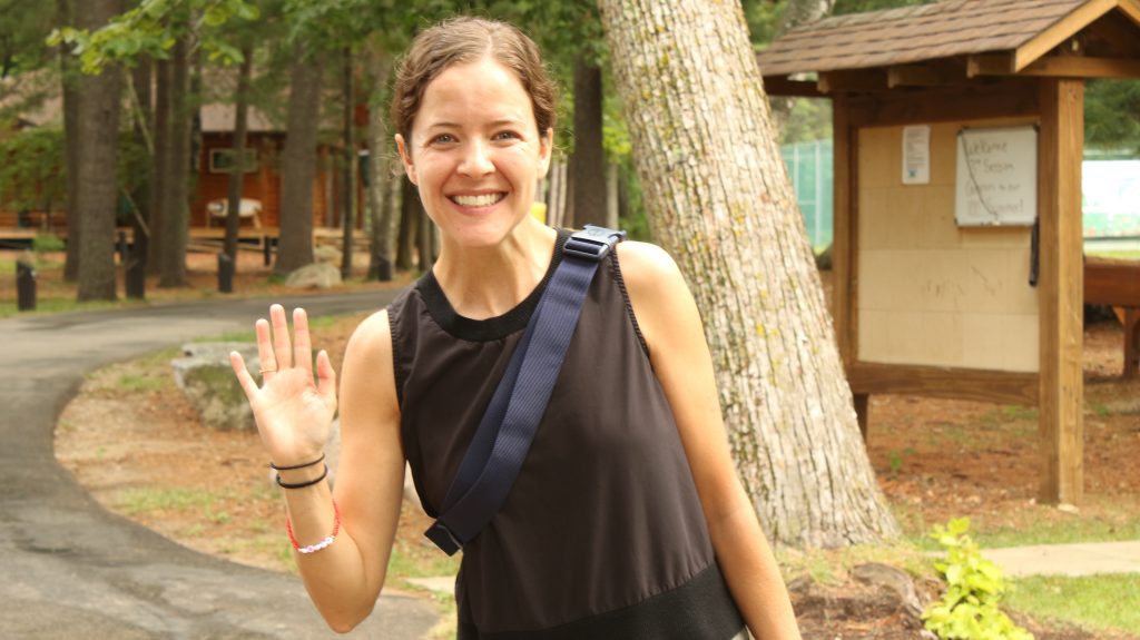 A camper coordinator at camp Foley waves and smiles at the camera