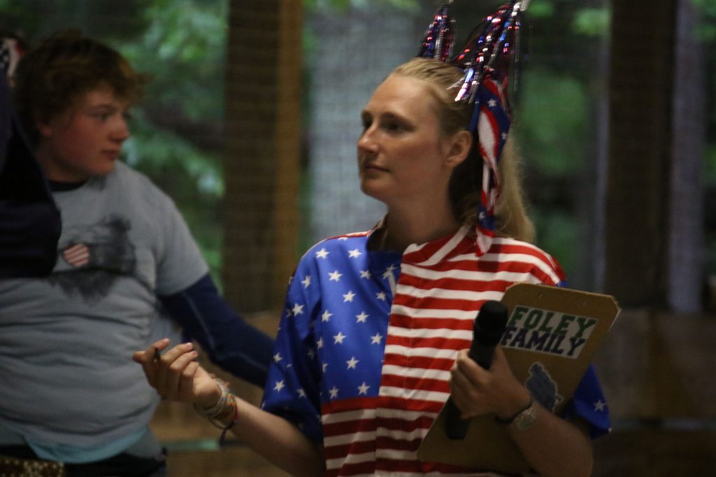 A woman in a American flag onesie holds a clipboard 