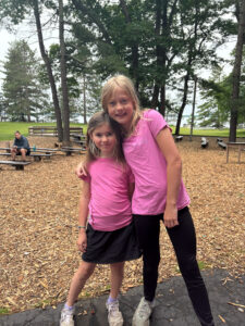 two camp Foley camper girls in pink shirts pose with arms around it each other and smiling at the camera 