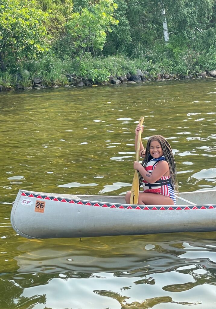 A young girl camper sits in a canoe holding a paddle at Camp Foley 