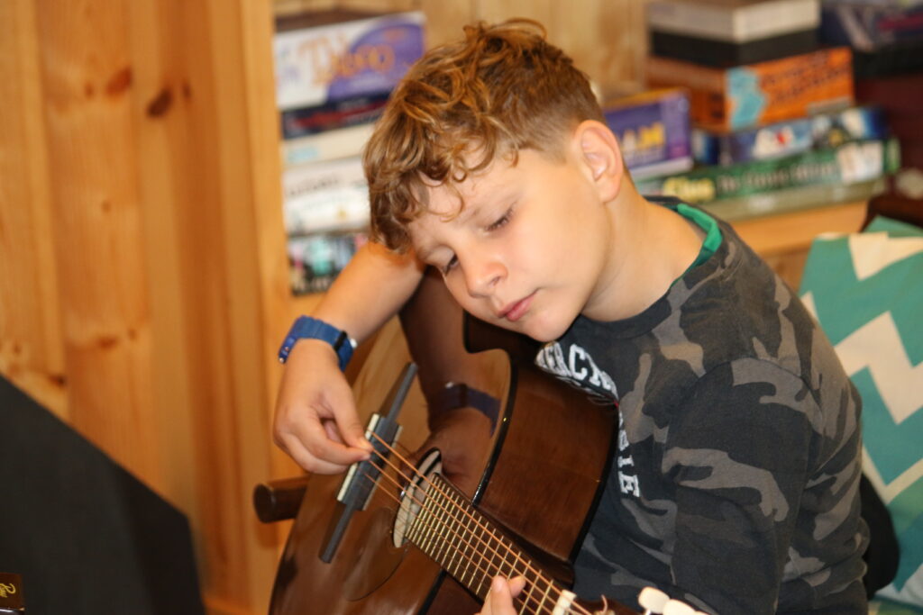 a child looks down as he plays the guitar at Camp Foley 