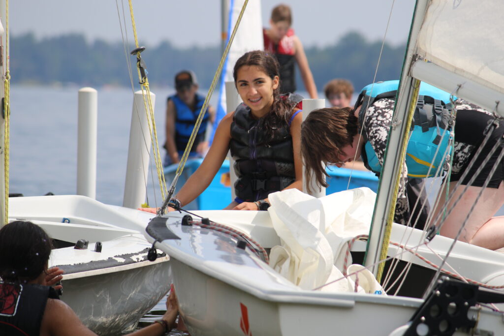 A girl Camp Foley camper at Foley stands on a sail boat and looks at the camera 