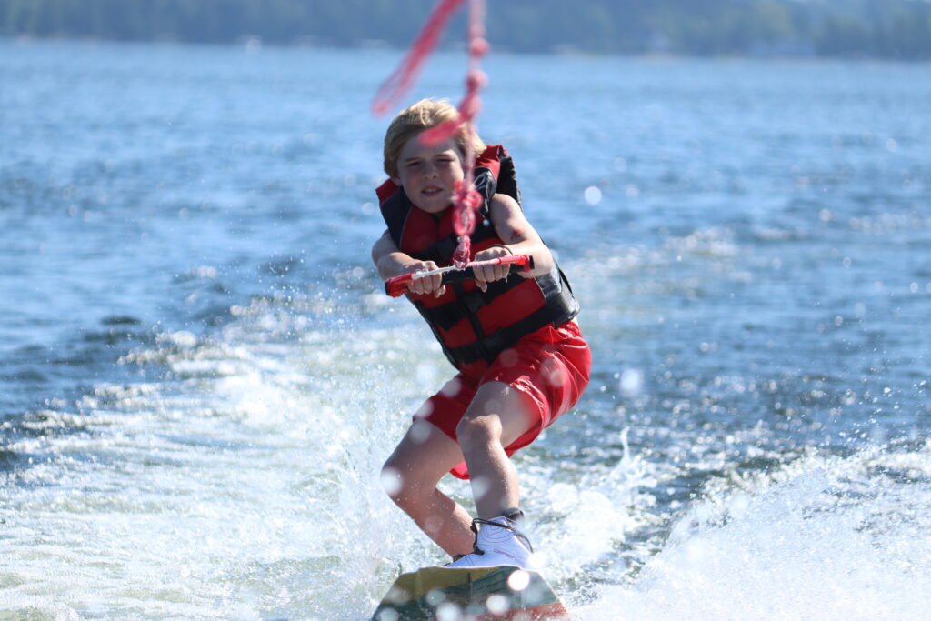 a young boy camper stands up on a wakeboard in Whitefish Lake at Camp Foley