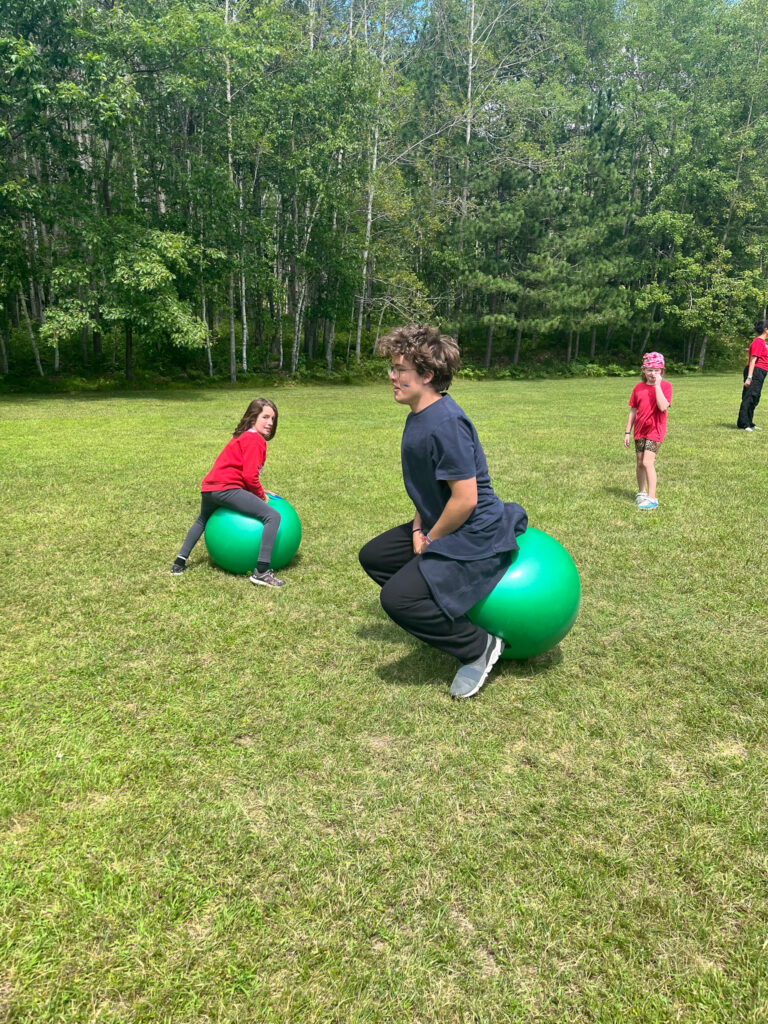 Campers at Camp Foley bounce on large hippity hop balls in a large field