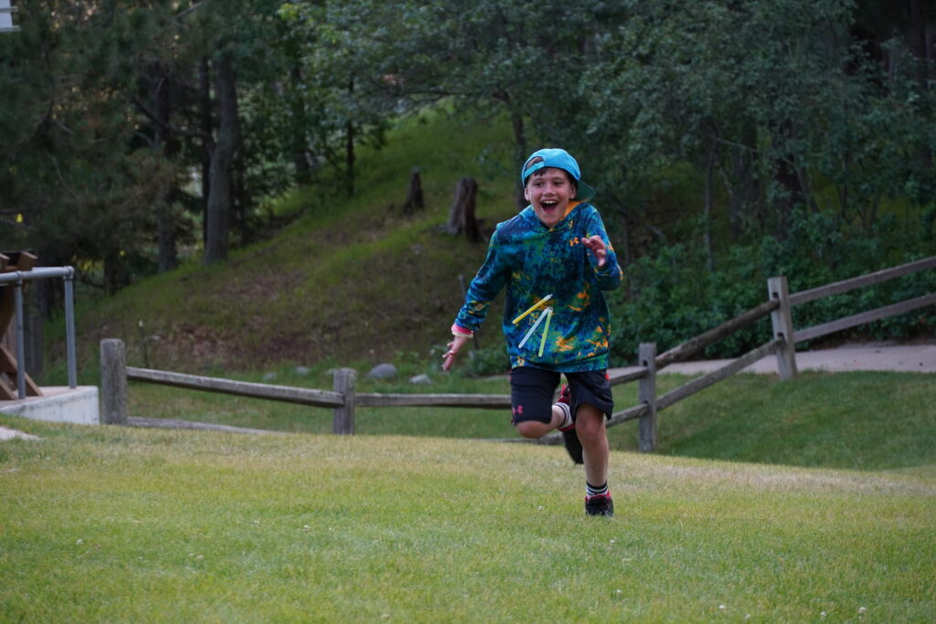 a boy camper at Camp Foley runs in a field with a smile on his face.