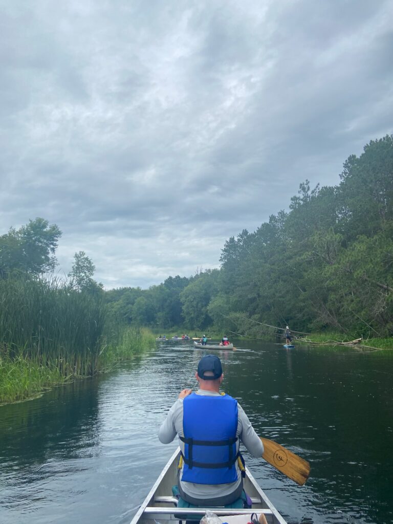 A Camp Foley trip leader paddles in the front of a canoe along the crow wing river