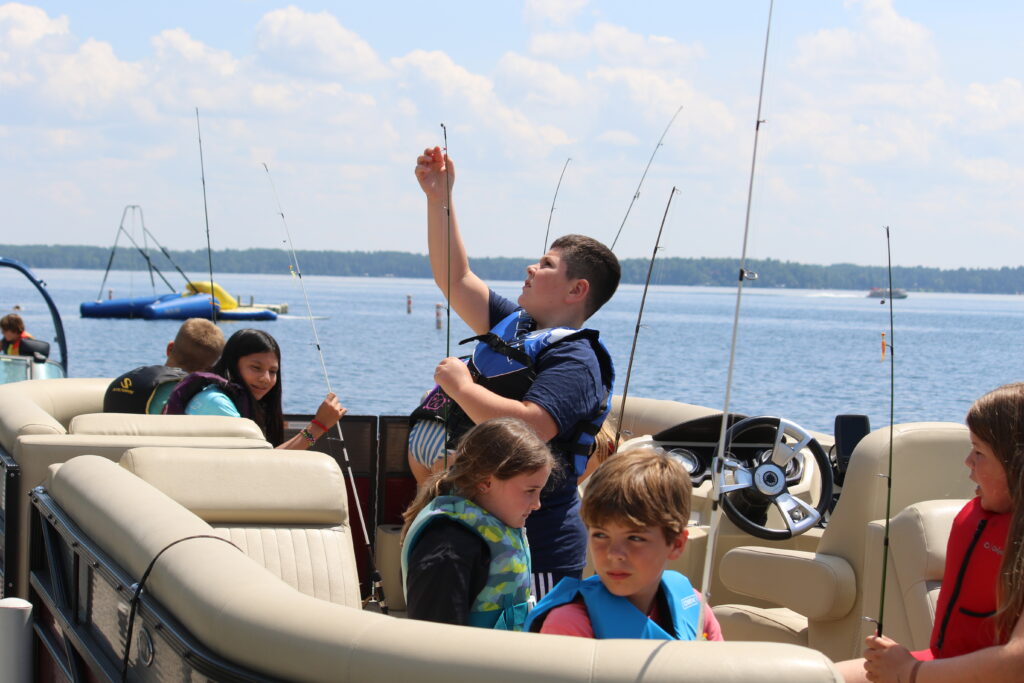 Campers at Camp Foley sit on a pontoon boat and hold fishing poles