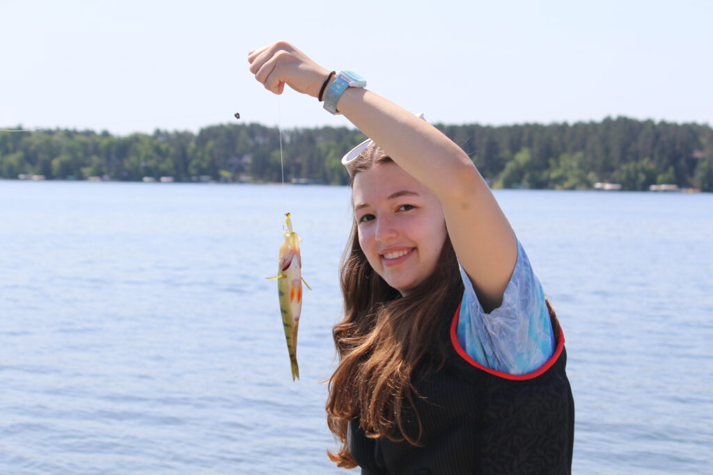 A brunette girl camper at Camp Foley holds up a fish on a hook 