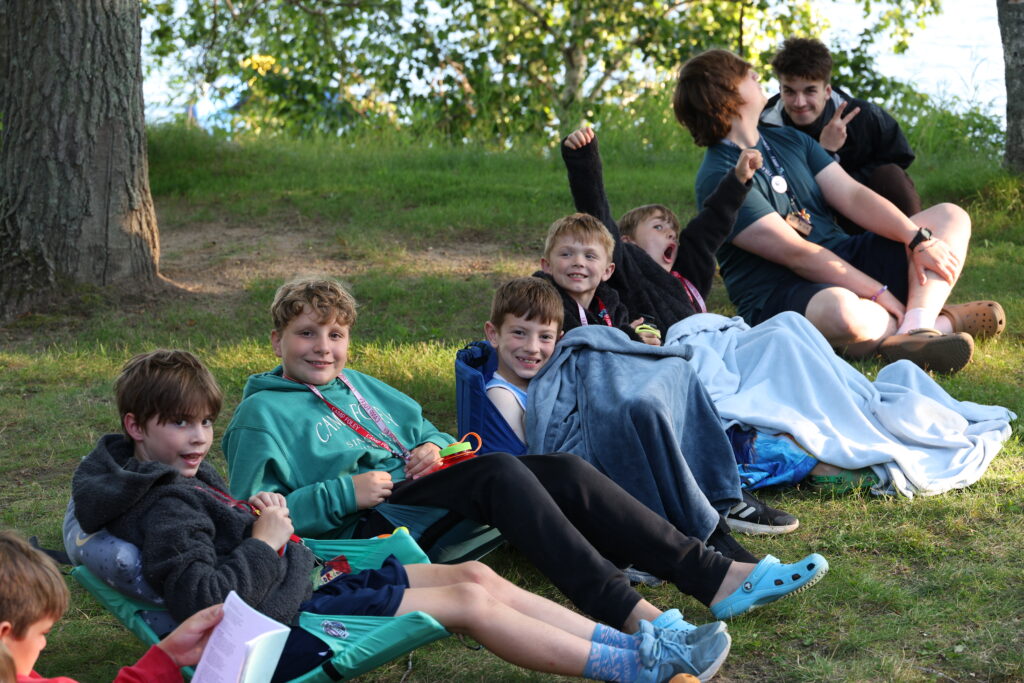 a group of boy Camp Foley campers sits on the ground together in camp chairs smiling at the camera